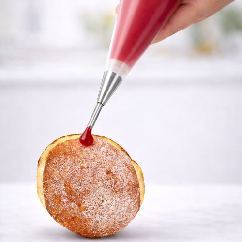 moment nadziewania pączka czerwonym nadzieniem przy użyciu rękawa cukierniczego z tylką