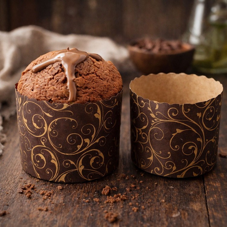 Czekoladowa babka panettone w ozdobnej papierowej formie ze złotymi ornamentami obok pustej formy