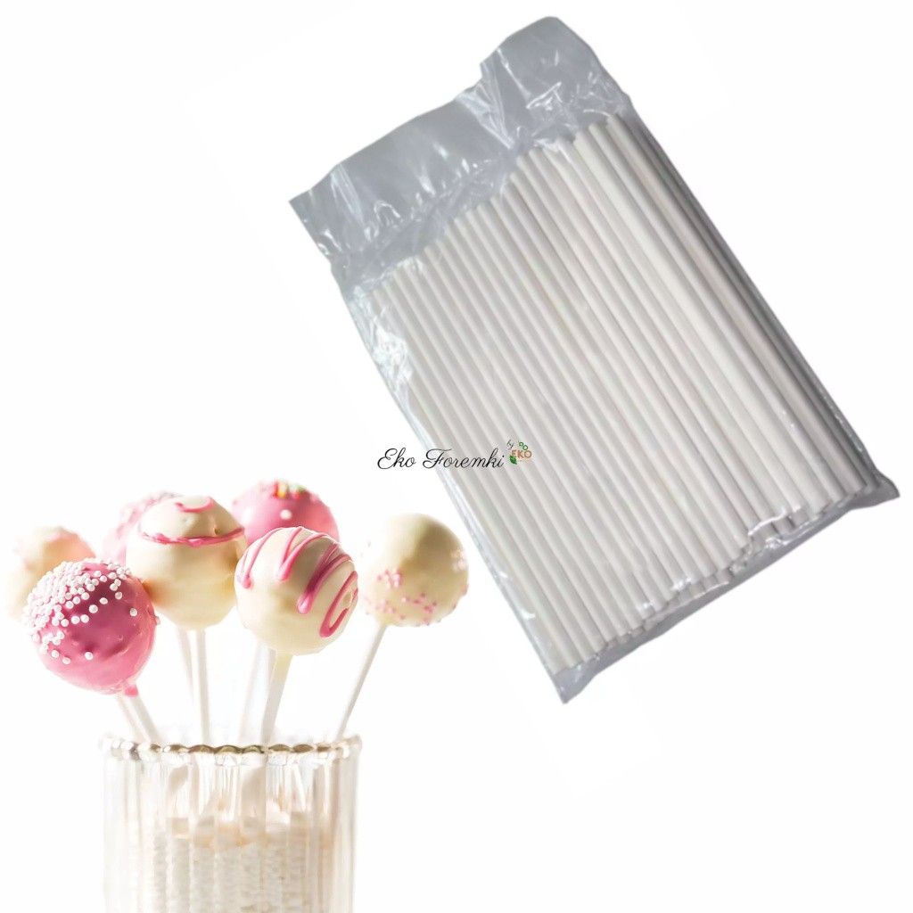 Białe patyczki do cake pops w opakowaniu, a obok kilka gotowych cake popsów na patyczkach, ozdobionych różową i białą polewą oraz posypką.