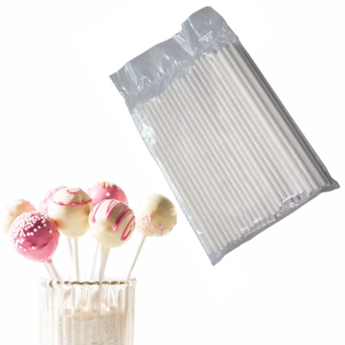 Patyczki do cake pops w opakowaniu oraz gotowe cake popsy udekorowane różową i białą polewą.