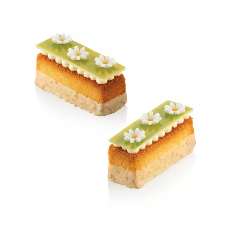 Dwie prostokątne monoporcje wykonane w formie Silikomart Mini Cake, z warstwami ciasta i zieloną dekoracją z białymi kwiatkami na wierzchu.