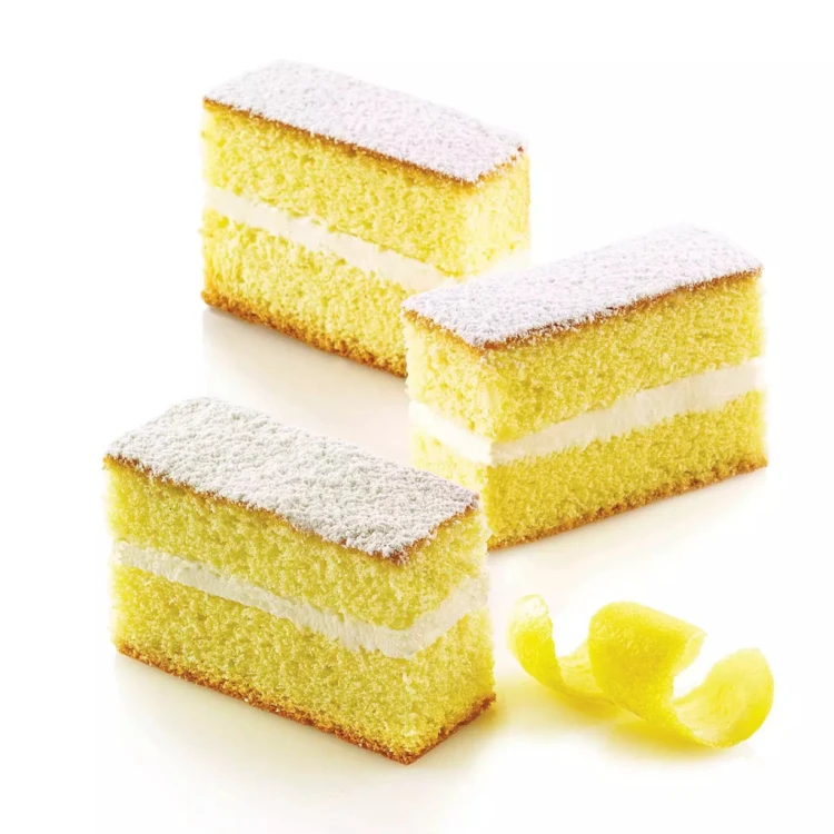 Trzy prostokątne mini ciasta z warstwami biszkoptu i kremu, wykonane w formie Silikomart Mini Cake, posypane cukrem pudrem i ozdobione skórką cytryny.